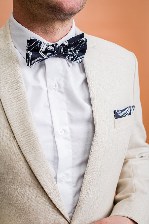 Elegant bow tie adorned with an intricate design of Australian native flora, showcasing a blend of green, brown, and yellow hues on a light background, perfect for special occasions
