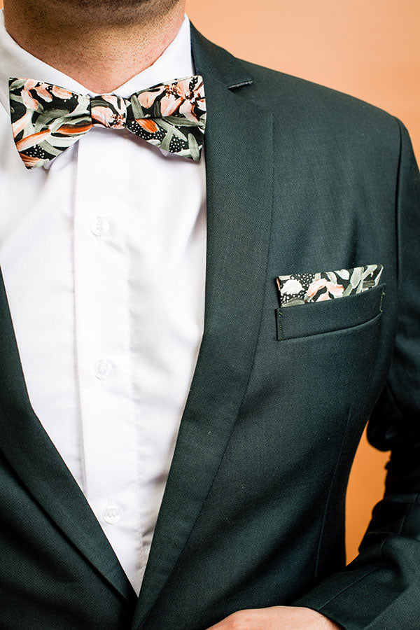 Elegant bow tie with an intricate protea design, showcasing lush green petals with vibrant pink centers and cream accents, perfect for enhancing formal attire with a sophisticated botanical touch