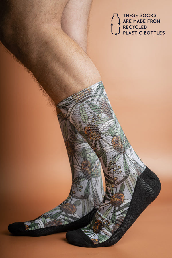 Eco-friendly grey socks featuring a unique Banksia pattern in shades of green, white, and burnt orange, made from recycled materials