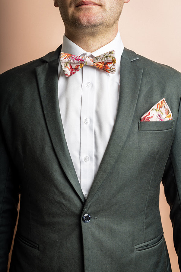 Bow tie featuring a detailed botanical print with green, yellow, and orange leaves and foliage, highlighting the diversity and beauty of various plant species on a dark background
