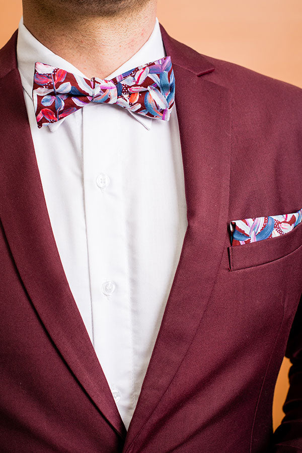 Modern and stylish bow tie featuring a detailed protea print in rich burgundy, complemented by shades of pink and green, inspired by the vibrant beauty of this flower